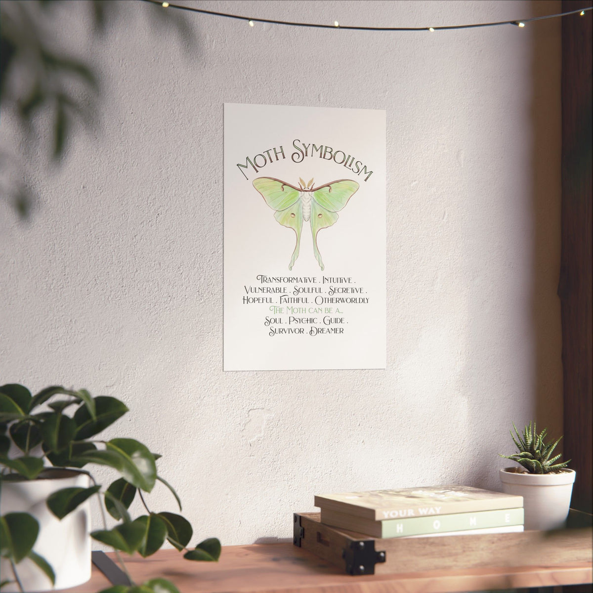 A vertical wall art print featuring a green luna moth illustration and the text 'Moth Symbolism' with meanings below, displayed on a textured wall in a styled room with plants and a wooden shelf.