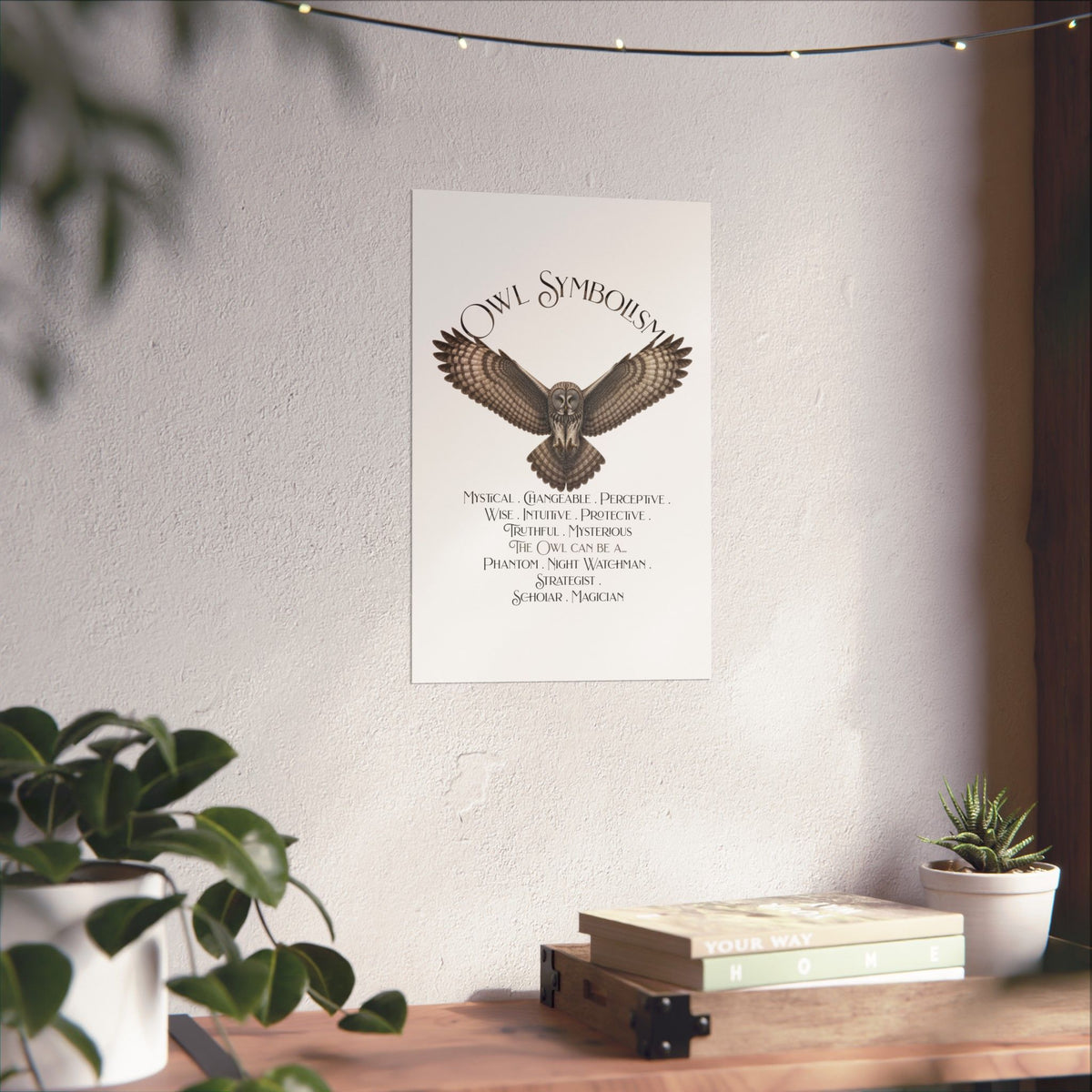 A vertical white art print featuring an owl illustration and the text 'OWL SYMBOLISM' hanging on a textured white wall above a wooden shelf with books and plants.