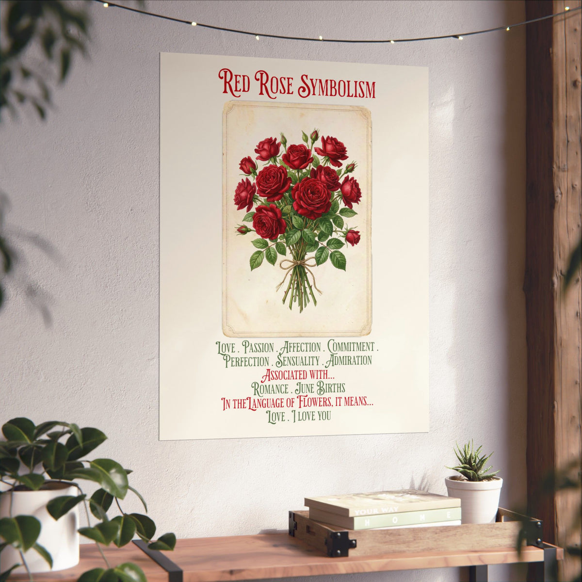 A vertical wall art print featuring a vintage-style illustration of red roses with the text 'RED ROSE SYMBOLISM' and romantic definitions beneath, displayed on a light wall above a wooden console with plants and books.