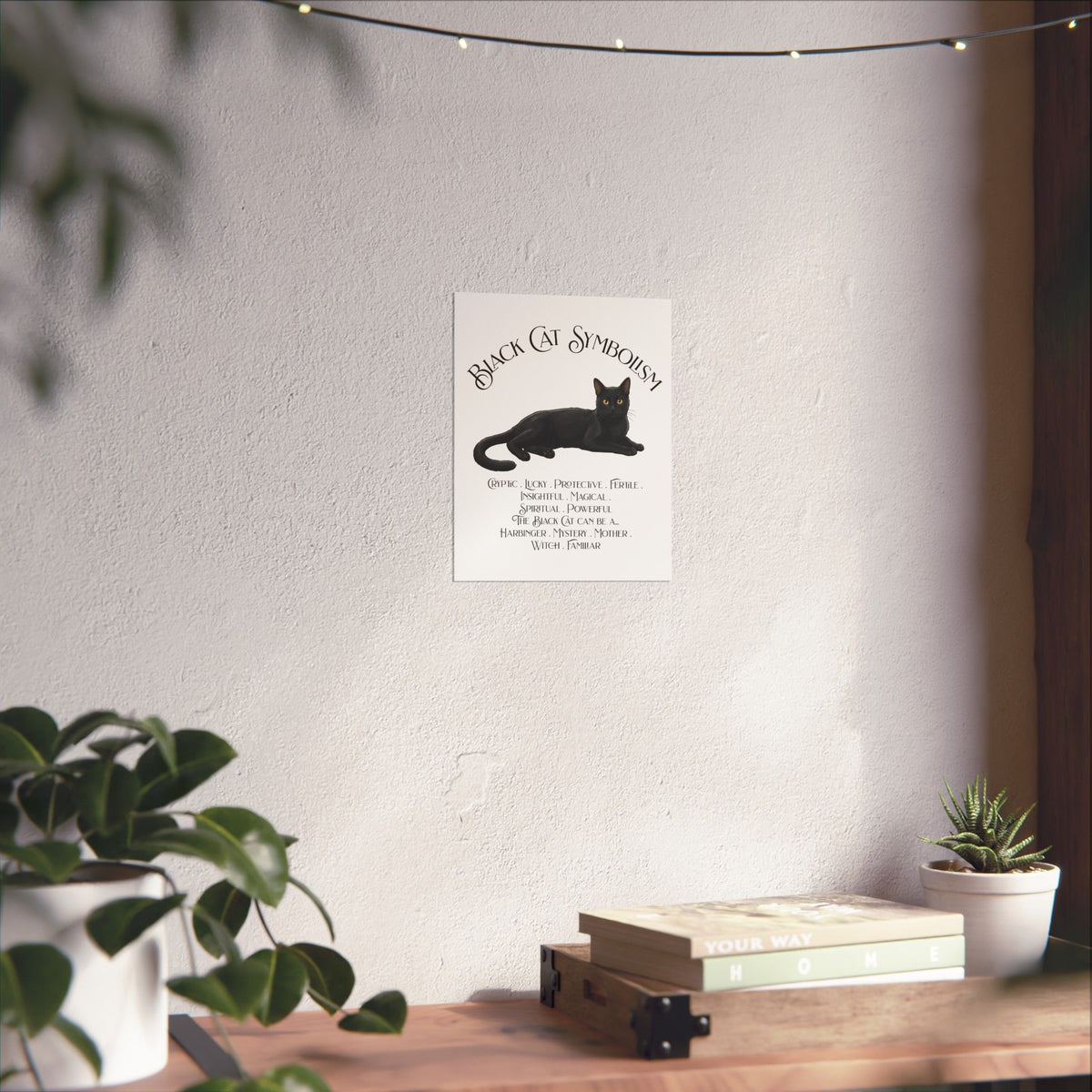 A vertical white art print featuring a black cat illustration and the text 'Black Cat Symbolism' displayed on a wall in a styled room setting with plants and a wooden shelf.
