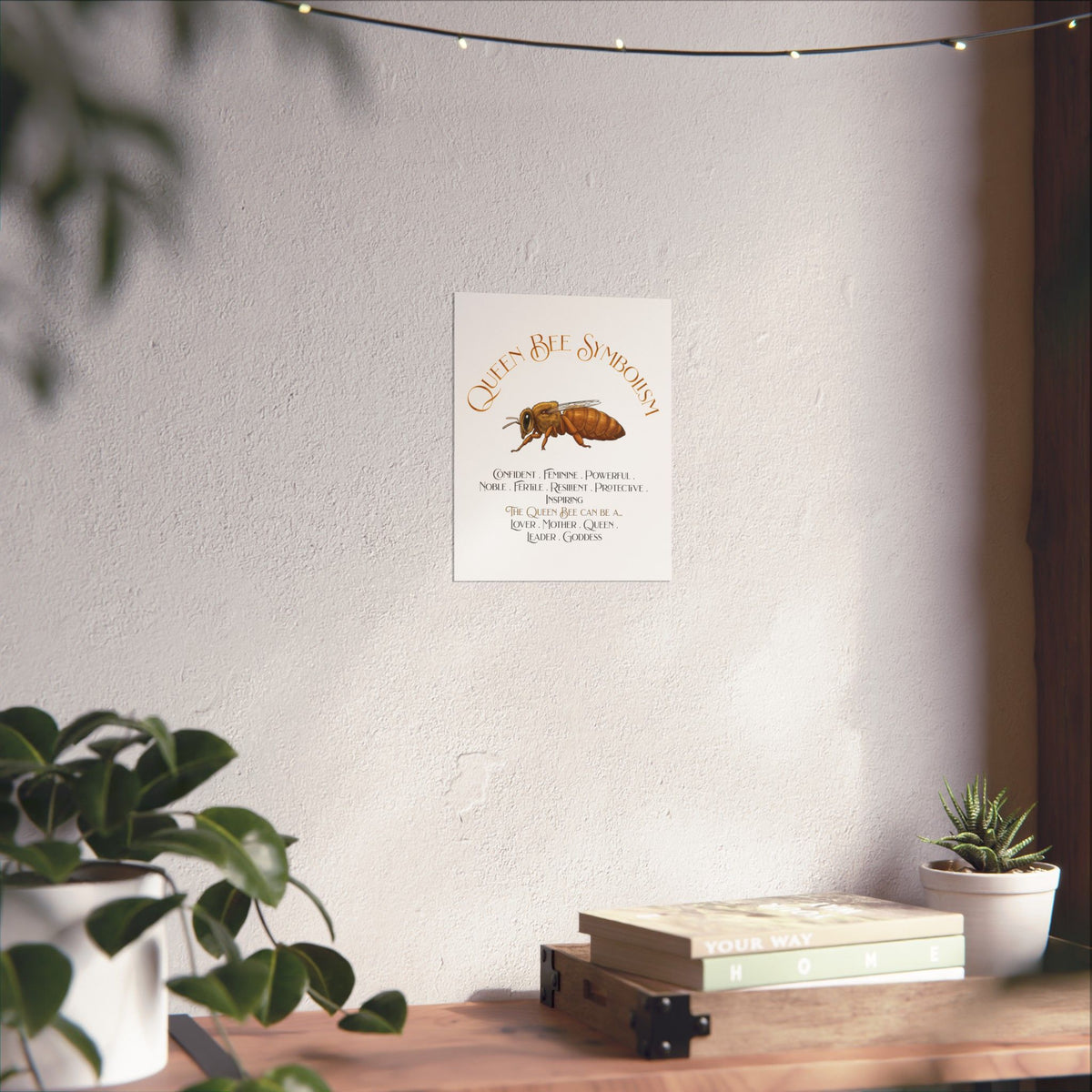A vertical wall art print featuring a watercolor-style queen bee and the text 'Queen Bee Symbolism' with a list of qualities and roles, displayed on a light wall above a wooden shelf with plants and books.