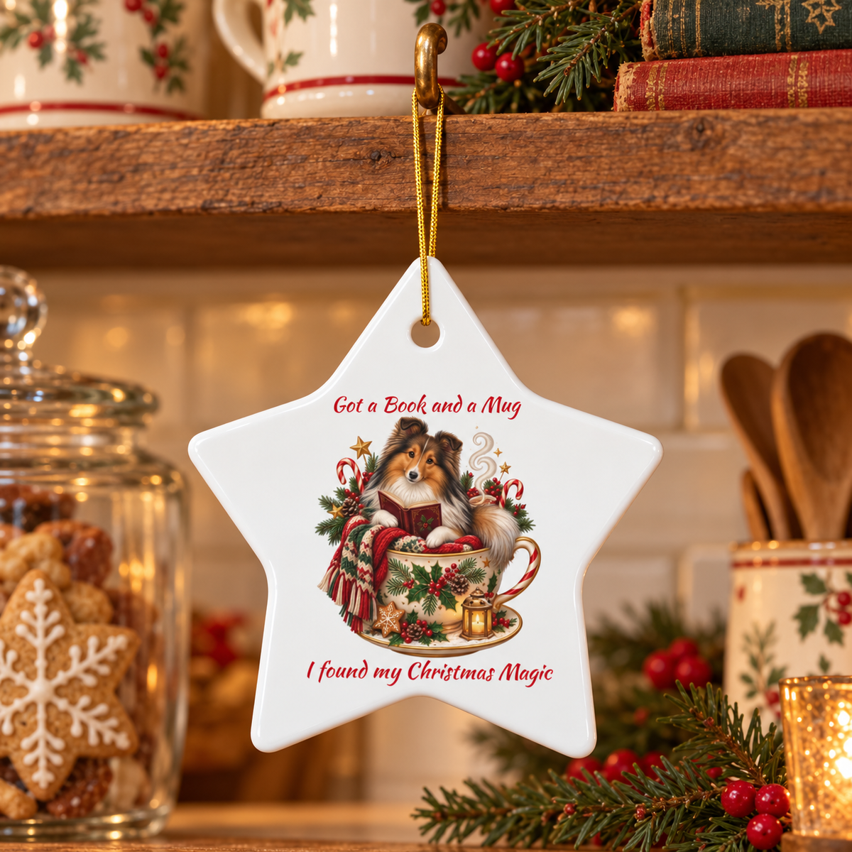 A white star-shaped ceramic Christmas ornament hanging from a gold loop on a wooden shelf. The ornament features a cozy illustration of a Sheltie in a teacup with red holiday accents and the text 'Got a Book and a Mug I found my Christmas Magic'.