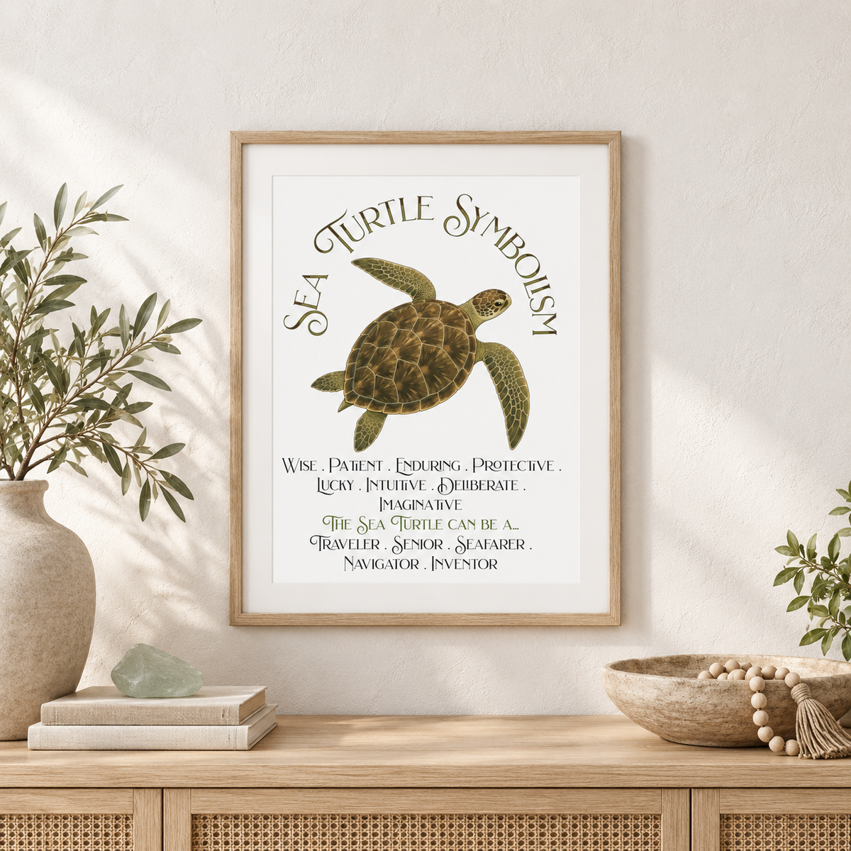 A framed art print featuring a sea turtle symbol and the words 'SEA TURTLE SYMBOLISM' with descriptive text below, displayed on a light wall above a wooden console table with a bowl of wooden Buddhist prayer beads, decorative plants, and books.