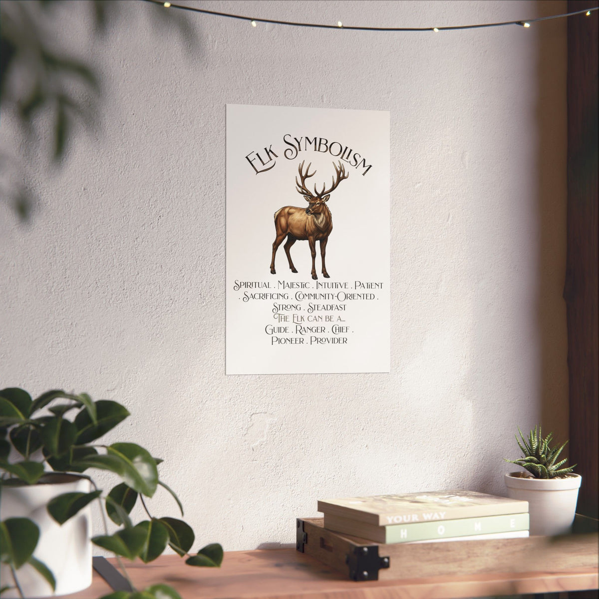 A vertical wall art print featuring a brown elk silhouette and the words 'Elk Symbolism' with smaller text beneath, displayed on a textured white wall above a wooden shelf with books and plants.