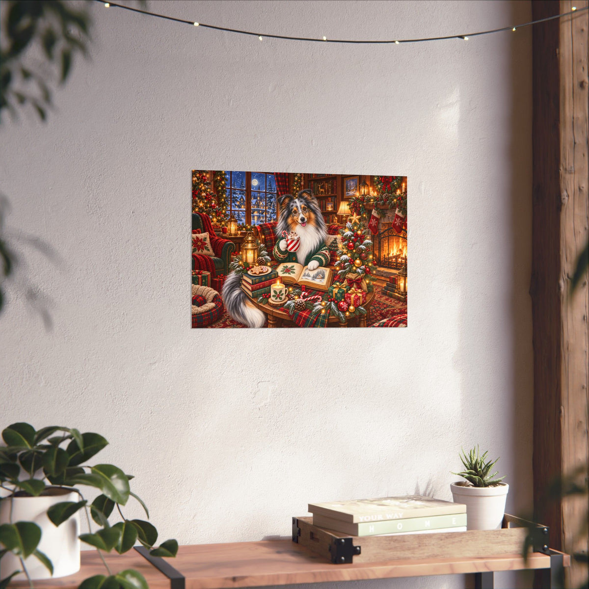 A rectangular wall art print showing a cozy Christmas scene with merle sheltie, displayed on a textured off-white wall above a wooden table with books and a small plant.