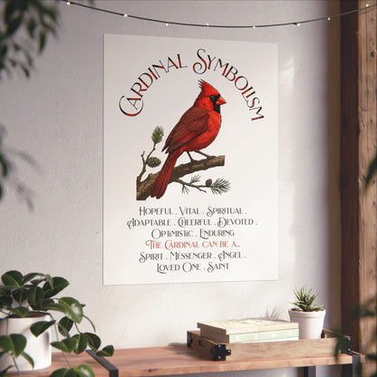 A vertical wall art print featuring a red cardinal on a pine branch with the title 'Cardinal Symbolism' and a list of cardinal qualities and meanings, displayed on a light wall above a wooden shelf with books and plants.