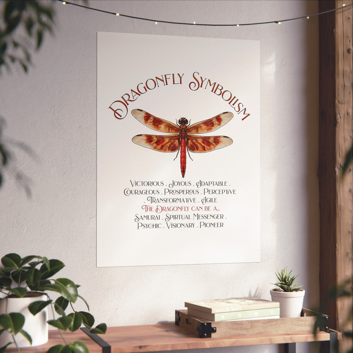 A vertical wall art print featuring a dragonfly illustration and the text 'Dragonfly Symbolism' displayed in a styled interior setting with plants and a wooden shelf.