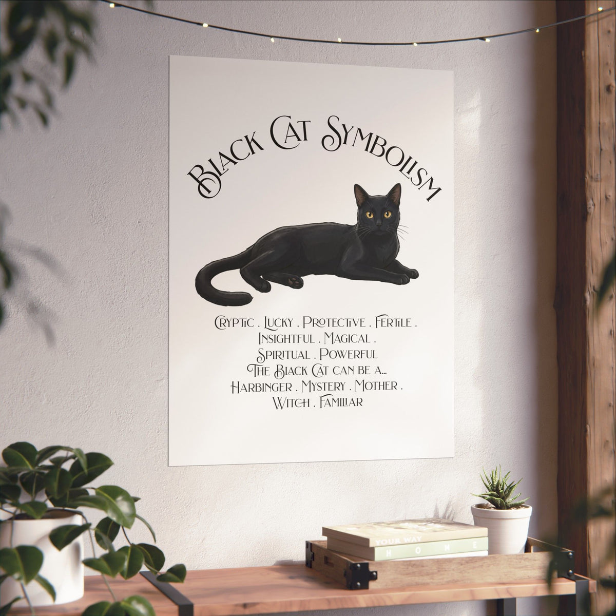 A vertical white art print featuring a black cat illustration and the text 'Black Cat Symbolism' displayed on a wall in a styled room setting with plants and a wooden shelf.