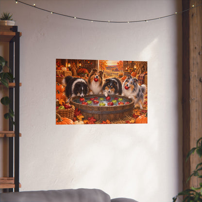 A rectangular wall art print showing four shelties bobbing for apples in an autumn harvest barn, displayed on a white wall above a sofa with string lights and plants visible in the room.