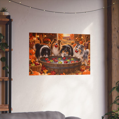 A rectangular wall art print showing four shelties bobbing for apples in an autumn harvest barn, displayed on a white wall above a sofa with string lights and plants visible in the room.