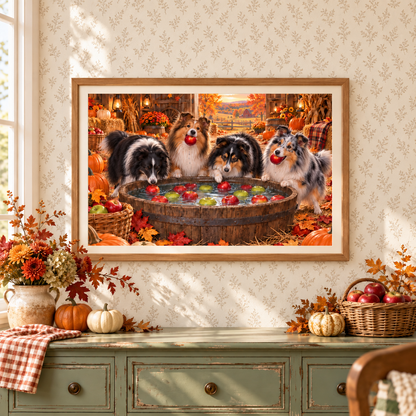 A framed art print depicting four Shelties bobbing for apples in a barrel, displayed on a wall with white leaf pattern wallpaper above a green console table decorated with autumn flowers, pumpkins, and baskets of apples.