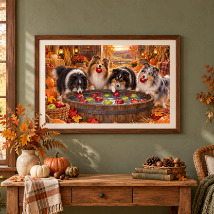 A framed wall art print showing four Shetland Sheepdogs bob for apples in an autumn barn scene, displayed on a green wall above a wooden console table with a vase of fall leaves, pumpkins, books, a orange and beige hand towel, and a basket of nuts. A woven chair with a blanket and pillow sits nearby.