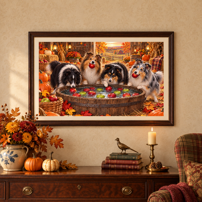 A framed wall art print depicting four shelties bobbing for apples in an autumn barn, displayed on a pale golden wallpaper above a mahogany console table with a vase of marigolds and fall leaves, stack of books, a brass bird figure, and a lit candle on a brass stand. A plaid chair with a burgundy blanket and a red and gold leaf patterned pillow sits nearby.