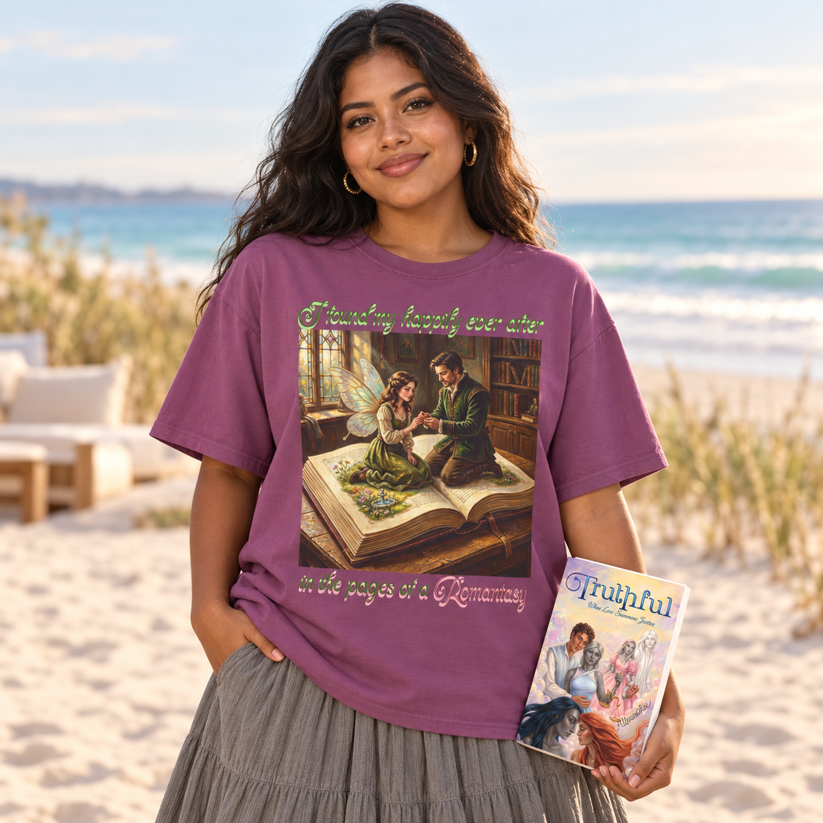 A woman stands on a beach wearing a purple graphic T-shirt with an open book where a man proposes to his fairy girlfriend and the words 'I found my happily ever after in the pages of a Romantasy' on the front, while holding a book called Truthful. The background shows sand, beach grass, ocean, and sky.
