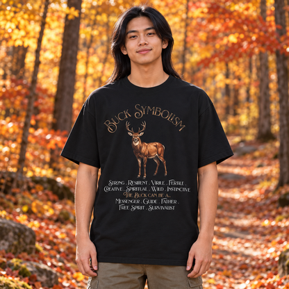 A man wearing a black graphic t-shirt with a brown deer and 'Buck Symbolism' text, standing in an autumn forest with orange leaves.
