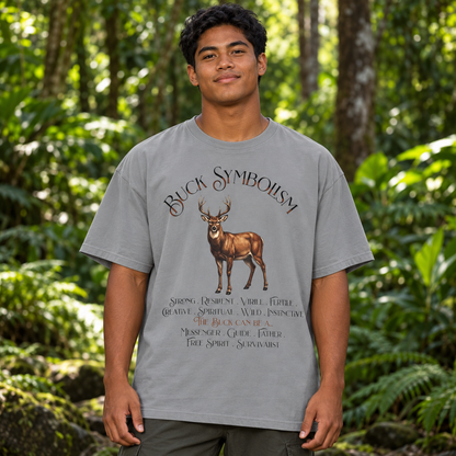 A man wearing a light gray graphic t-shirt with a deer design and the text 'Buck Symbolism' in a forest setting.