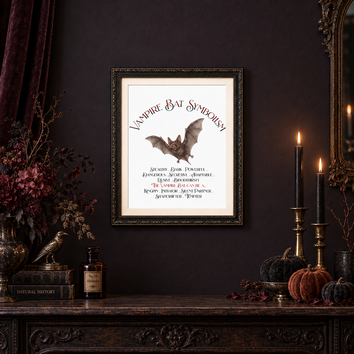 A framed gothic art print titled 'Vampire Bat Symbolism' featuring a bat illustration and text, displayed on a dark wall above a decorated mantel with candles, pumpkins, and dried flowers.