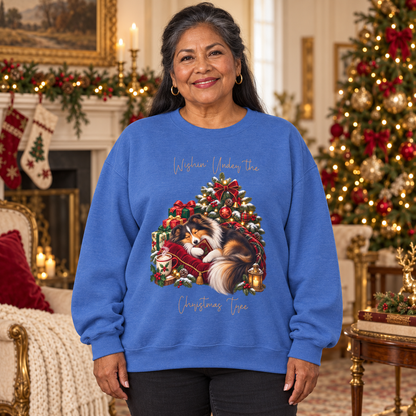 A woman wearing a royal blue crewneck sweatshirt with a festive Christmas graphic of a fluffy dog curled on a red velvet bed under a decorated Christmas tree. The text on the sweatshirt reads, 'Wishin' Under the Christmas Tree'.