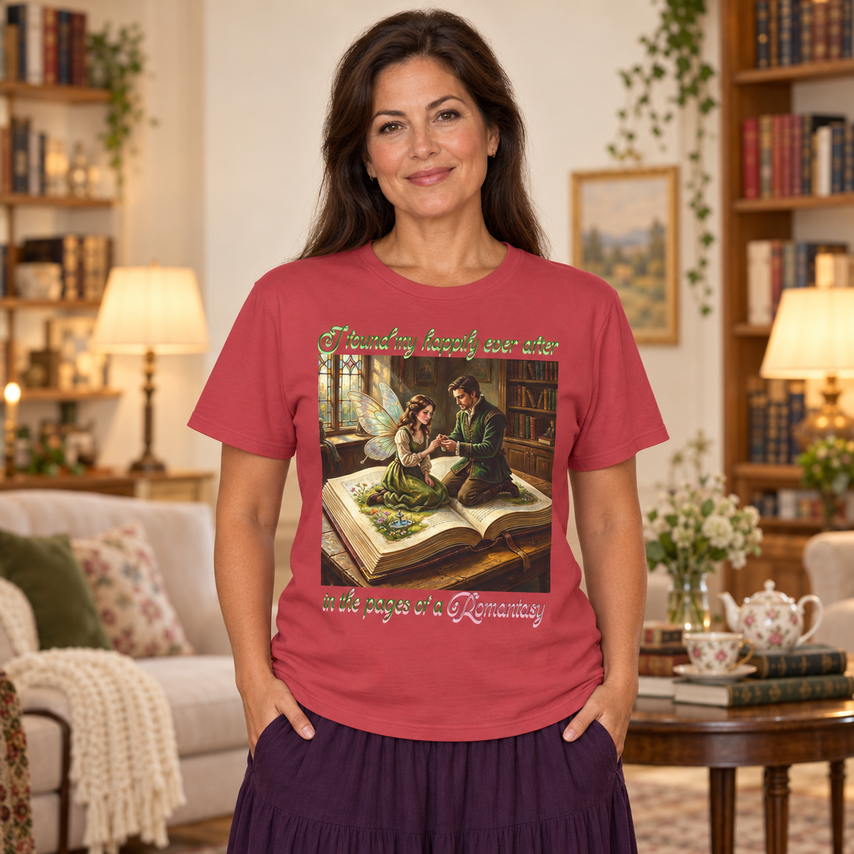 A woman wearing a dusty red graphic t-shirt with a vintage-style illustration of a fairy and a man sitting on an open book. The t-shirt features the text 'I found my happily ever after in the pages of a Romantasy'.
