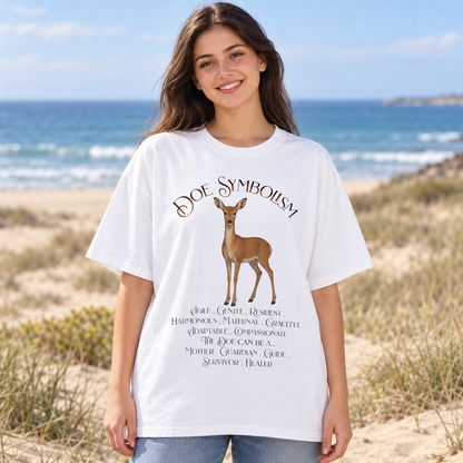 A woman standing on a beach wearing a white graphic T-shirt with a deer illustration and the text 'DOE SYMBOLISM' and additional decorative text below.