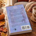 The back cover of Faithful by Allexandra rests on a wood table surrounded by autumn leaves, a vase of flowers, a pumpkin, and a coffee mug. In the background is a chair with a knit blanket.