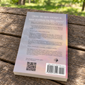 The back of Fated, resting on a weathered wooden park table with a blurred green park background.