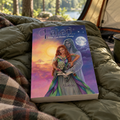 'Fated: When Love Becomes Destiny' by Alexandra lies on an olive green sleeping bag inside a tent, with a forest and lake visible in the background.
