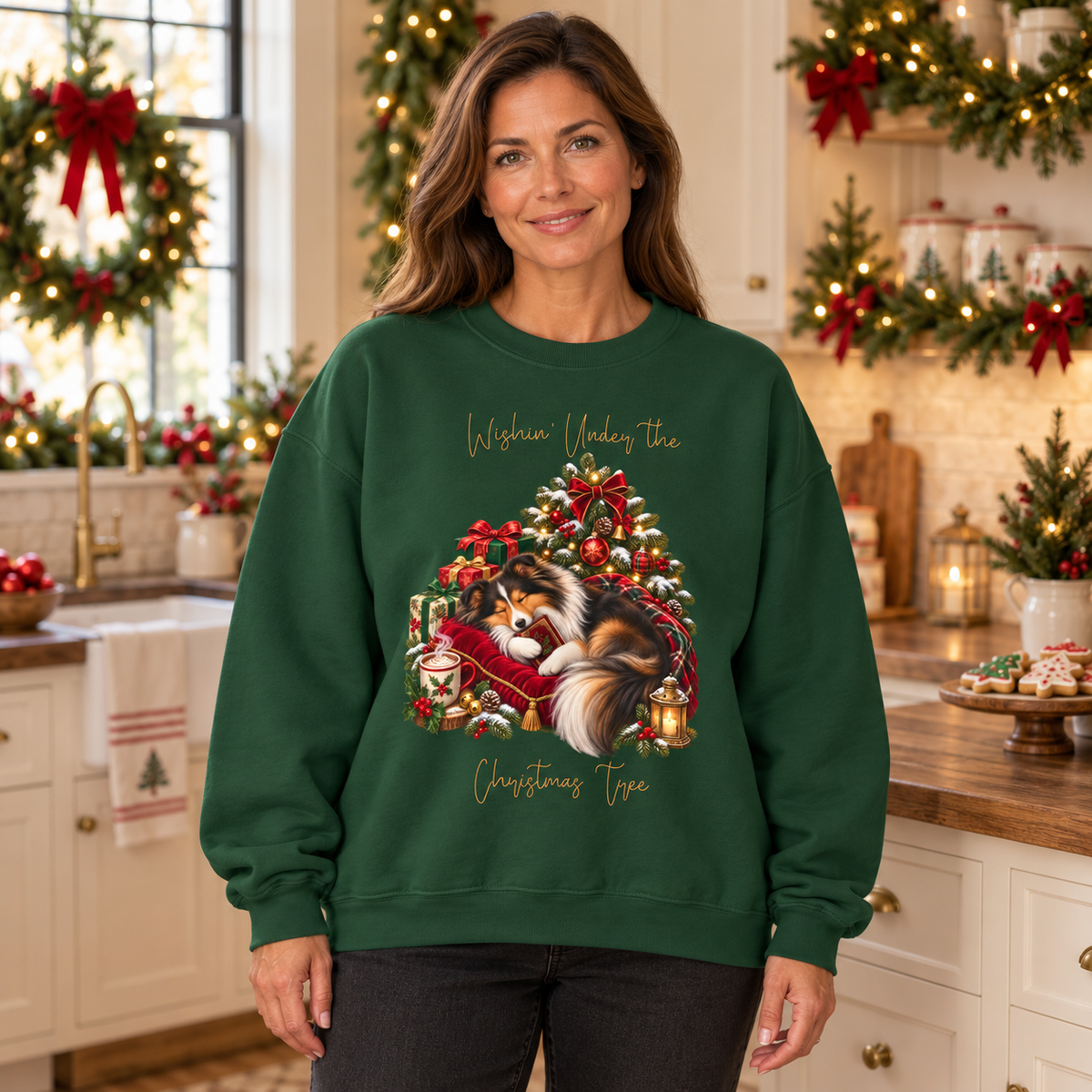 A woman wearing a dark green sweatshirt with a sheltie sleeping beside a festive Christmas tree and the text 'Wishin' Under the Christmas Tree' stands in a decorated holiday kitchen.