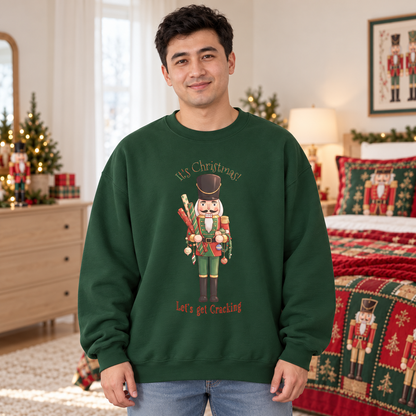 A man wearing a dark green crewneck sweatshirt with a nutcracker holding wrapping paper and decorations surrounded by the text 'It's Christmas! Let's get Cracking' in a decorated holiday bedroom setting.