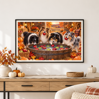 A framed wall art print showing four shelties bobbing for apples in an autumn harvest barn, displayed above a console table with pumpkins, a flat woven basket, books, and a white vase of fall leaves in a modern styled interior.