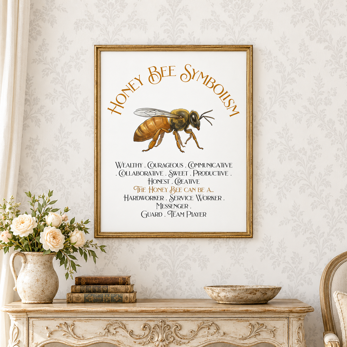 A framed art print featuring a honey bee illustration and the text 'Honey Bee Symbolism' with associated qualities, displayed on a white patterned wallpaper wall above a vintage-style console table with flowers, a flat bowl, and books.
