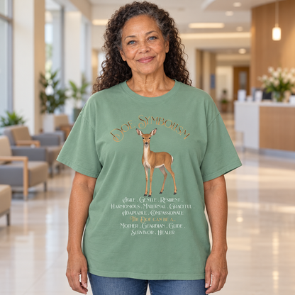 A woman wearing a sage green graphic t-shirt with a deer illustration and the text 'Doe Symbolism' in a hospital lobby.