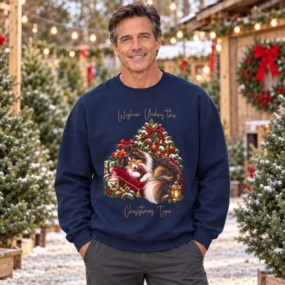 A smiling man wearing a navy blue crewneck sweatshirt with a festive Christmas graphic of a fluffy dog under a decorated tree. The graphic includes the text 'Wishin' Under the Christmas Tree'.