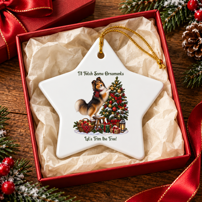 A white star-shaped ceramic Christmas ornament with a gold hanging loop, displayed inside a red gift box with tissue paper. The ornament features an illustration of a sable sheltie decorating a Christmas tree surrounded by the text 'I'll Fetch Some Ornaments' and 'Let's Trim the Tree!'.