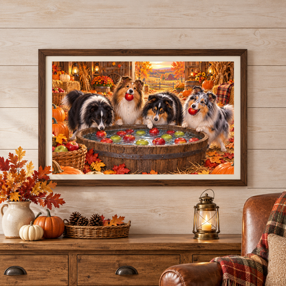 A framed wall art print showing four shelties bobbing for apples, displayed in a cozy autumn-themed barn on a white wood wall above a wooden console table with pumpkins, a lantern, a basket of pinecones, and a leather armchair.