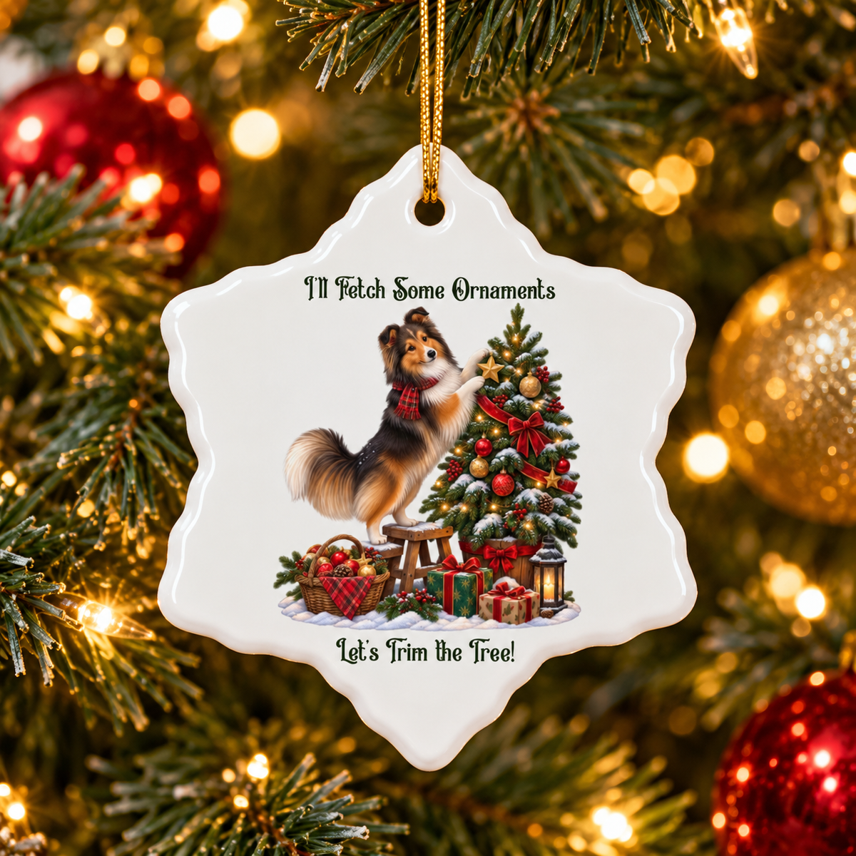 A white ceramic Christmas ornament shaped like a snowflake hangs from a gold string in front of a lit Christmas tree. The ornament features an illustration of a fluffy sable sheltie standing on its hind legs while decorating a Christmas tree, with the text 'I'll Fetch Some Ornaments' at the top and 'Let's Trim the Tree!' at the bottom.