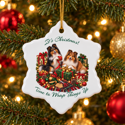 A white snowflake-shaped Christmas ornament hanging on a decorated tree branch. The ornament features an illustration of two shelties surrounded by wrapped gifts, ornaments, and lights, with the text 'It's Christmas! Time to Wrap Things Up'.
