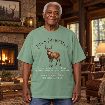 An older man wearing a sage green graphic t-shirt with a deer design and the text 'Buck Symbolism' and its symbolic meanings printed on the front. The man stands in a rustic lodge living room.