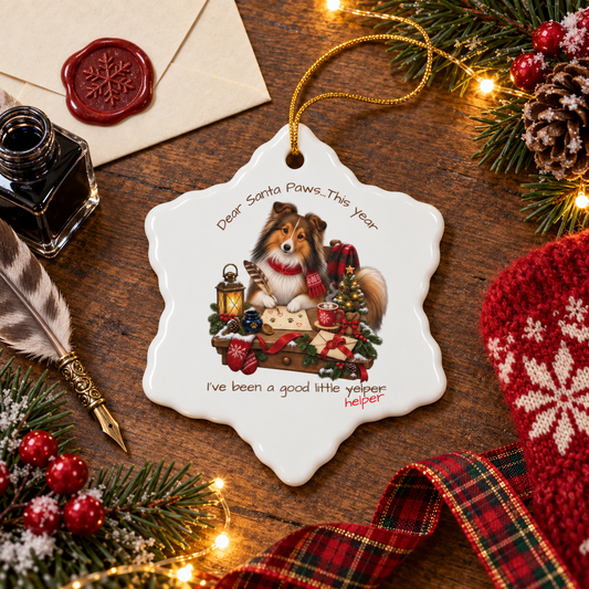 A snowflake-shaped ceramic Christmas ornament featuring a Sheltie dog illustration and the text 'Dear Santa Paws...This year I've been a good little yelper." The last word is crossed out and replaced with 'helper'.