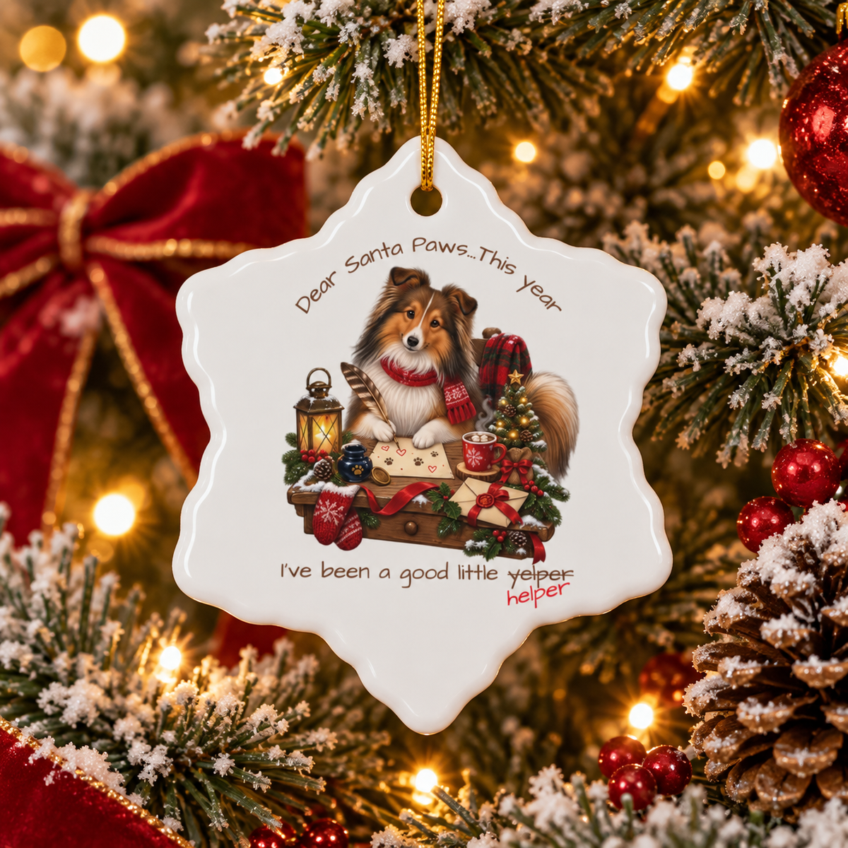 A white snowflake-shaped Christmas ornament hanging on a decorated tree. The ornament features an illustration of a Sheltie sitting at a table with a lantern, gift box, and holiday decorations, with the text 'Dear Santa Paws...This year I've been a good little yelper'. The last word is crossed out and replaced with 'helper'.