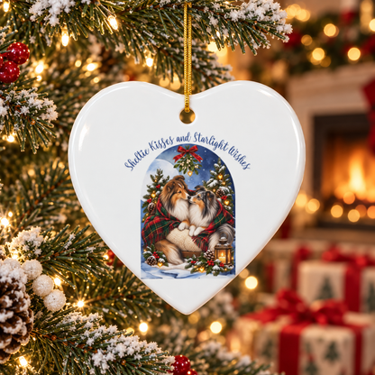 Heart-shaped Christmas ornament hanging on a decorated tree, featuring an illustration of two Sheltie dogs kissing under a blue night sky with mistletoe and a red and green plaid blanket. The ornament has a gold hanging loop and festive text reading 'Sheltie Kisses and Starlight Wishes'.