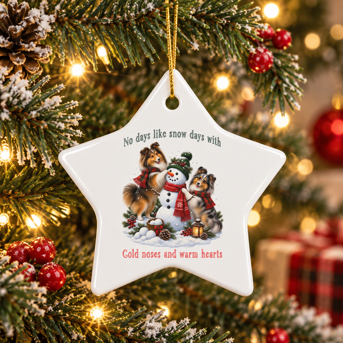 A white ceramic ornament shaped like a star hangs on a decorated Christmas tree. The ornament features an illustration of two dogs building a snowman and includes the text 'No days like snow days with' above and 'Cold noses and warm hearts' below.